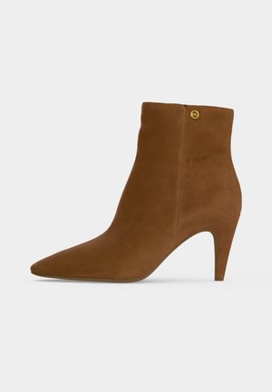 Brown suede pointed-toe ankle boot with a slim high heel and a small gold circular logo near the top edge.