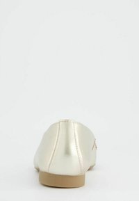 Metalická zlatá plochá bota s hladkým povrchem, zaobleným tvarem, minimálním podpatkem a béžovou podrážkou. Jednoduchý design bez viditelného hardwaru.