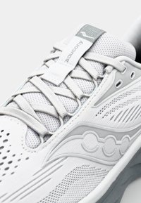 Baskets blanches avec une tige en maille, accents texturés gris, sections perforées pour la respirabilité et un logo de marque distinctif sur le côté.