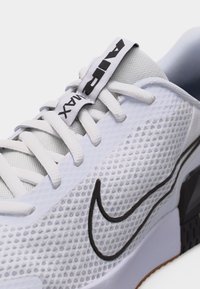 Λευκό αθλητικό παπούτσι Nike Air Max σε κοντινό πλάνο που δείχνει το υφασμάτινο πλέγμα με υφή, το μαύρο λογότυπο Swoosh και τα λευκά κορδόνια με τη σήμανση "AIR" στη γλώσσα.