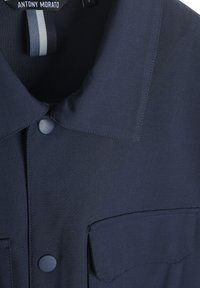 Marineblauw shirt met een kraag, sluiting met knopen aan de voorkant en twee borstzakken. Gemaakt van gladde stof met een subtiele textuur en een contrasterend binnenlabel.