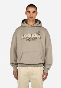 Beżowa bluza z kapturem na sznurki, dużą przednią kieszenią i kwiatowym wzorem na klatce piersiowej. Miękka tkanina z prążkowanymi mankietami i dołem.