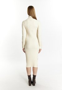 Knit dress in cream with vertical ribbing, turtleneck, long sleeves, and side slits; paired with brown platform ankle boots.