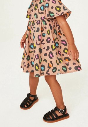 Robe rose avec un imprimé léopard coloré, manches courtes et taille froncée. Sandales noires à lanières avec une boucle et une semelle en caoutchouc.