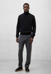 Schwarzer Rollkragenspullover, graue maßgeschneiderte Hose und schwarze Sneaker mit Gummisohlen. Schlichtes Design, taillierte Silhouette, strukturierter Strick.