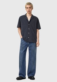 Lyhythihainen tummansininen paita kauluksella, hopeiset napit, yhdistetty löysiin sinisiin farkkuihin ja mustiin kenkiin. Minimalistinen tyyli.