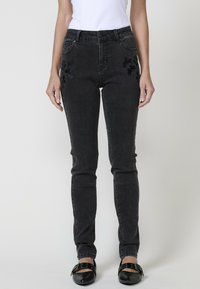 Juoda džinsinė kelnės su siauru siluetu, su išsiuvinėtais gėlių akcentais ant kišenių ir klasikinėmis penkių kišenių detalėmis.