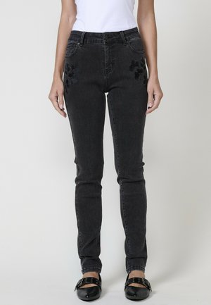 Jean en denim noir avec une coupe slim, présentant des accents floraux brodés sur les poches et un design classique à cinq poches.