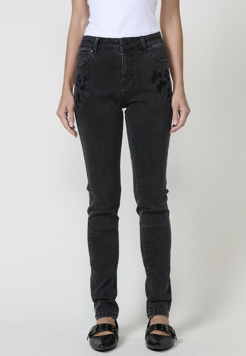 Juoda džinsinė kelnės su siauru siluetu, su išsiuvinėtais gėlių akcentais ant kišenių ir klasikinėmis penkių kišenių detalėmis.
