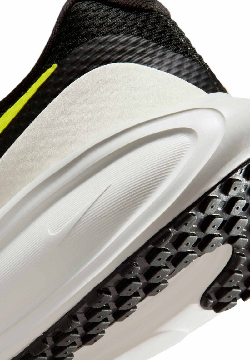 Zapatilla deportiva en blanco y negro con un upper texturizado, diseño elegante, destacado acento amarillo y una suela de goma con un patrón para mayor tracción.