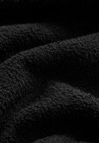 Měkká černá tkanina s texturovaným, načechraným povrchem, se různými výškami vlasu a hladkými sklady, které vytvářejí hloubku a stíny.