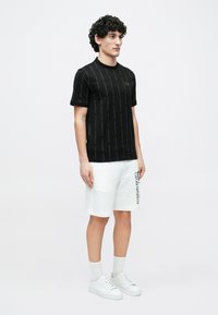 Czarny t-shirt z krótkim rękawem z pionowym wzorem logo, w zestawie z białymi szortami typu cargo z bocznym logo. Teksturowana tkanina, casualowy fason.