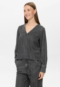 Top grigio in denim a maniche lunghe con scollatura a V, vestibilità morbida e orlo cucito. Abbinato a pantaloni in denim grigio coordinati, con una leggera texture.