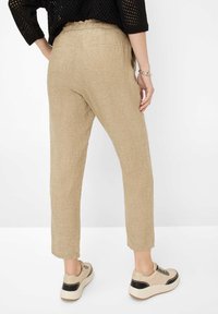 Pantalons en lin beige avec une coupe décontractée, taille élastique et poches arrière. Associés à des baskets de couleur claire avec un design texturé.