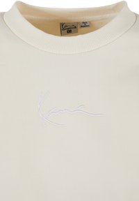 Svetlo béžová mikina so žebrovaným okrajom okolo krku. Na prednej strane má biele vyšívané logo. Vyrobená z jemného materiálu.