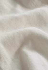 O țesătură texturată, de culoare alb-întunecată, arată fibre naturale moi cu un ușor luciu, creând pliuri și valuri delicate pe suprafață.