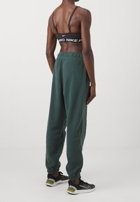 Svart sportbh med logotyp, gröna fleece-joggingbyxor med elastisk midja och muddar, ihop med svarta träningsskor med grå och gröna detaljer.