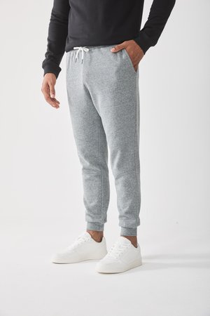 Gray fleece joggers with an elastic waistband and white drawstring, featuring side pockets and tapered cuffs, paired with white sneakers.