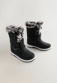 Czarne zimowe botki z pikowanymi bokami, białymi podeszwami i szarym sztucznym futrem wokół górnej części, stojące na jasnym tle.