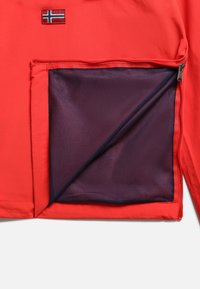 Tejido de chaqueta roja con un bolsillo con cremallera. El bolsillo tiene un forro de malla en color púrpura oscuro. Pequeña parche de bandera noruega en la parte superior izquierda.
