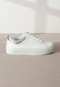 Adidași albi cu platformă, cu o parte superioară din piele netedă și accente metalice argintii la călcâi. Vârf rotund, șnururi minimaliste, talpă texturată.