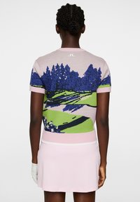 Sweter golfowy wykonany na drutach z różowym tłem i żywym przedstawieniem krajobrazu w odcieniach niebieskiego i zielonego. Posiada krótkie rękawy i dopasowany krój.