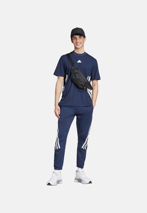 Marinefarbener Sportanzug mit einem kurzärmeligen Shirt mit weißen Streifen, passenden Hosen mit Streifenakzenten und einer schwarzen Umhängetasche.