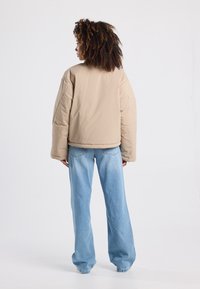 Beige puffer jacket with a boxy fit, wide sleeves, and a cropped hem, paired with light blue wide-leg jeans. Smooth texture, minimal stitching details.