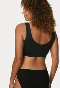 Svart sömlös bralette med breda axelband och rundad rygg. Slät textur, stretchig tyg, i kombination med matchande högmidjade trosor.