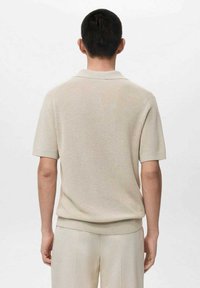 Beżowa koszulka polo z krótkim rękawem o prążkowanej fakturze, z płaskim kołnierzem i luźnym krojem, z subtelnym wykończeniem na wysokości talii.