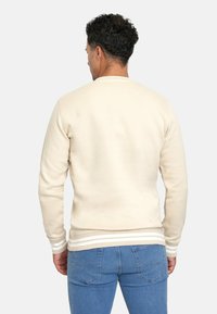 Sudadera de algodón beige con cuello redondo, puños acanalados y dobladillo con rayas blancas. La vista posterior muestra una textura suave y una forma ajustada.