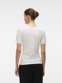 T-shirt bianca in cotone con scollatura rotonda e maniche corte, design aderente, texture liscia. Indossata con pantaloni neri, vista da dietro.