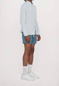 Světlomodrá košile s dlouhým rukávem a knoflíky, s kapsou, doplněná džínovými kraťasy, bílými teniskami a bílými ponožkami.