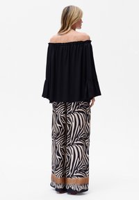 Schwarze schulterfreie Bluse mit Glockenärmeln, kombiniert mit weiten Hosen im beige-schwarzen Zebra-Muster und goldenen Säumen.