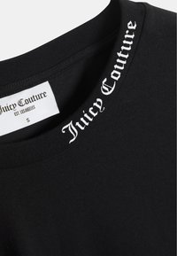 Mustast värvi ümara kaelusega pusa, millel on krae peal valge "Juicy Couture" tekst. Materjal tundub pehme ja sileda tekstuuriga. Suuremärgistus on nähtav.