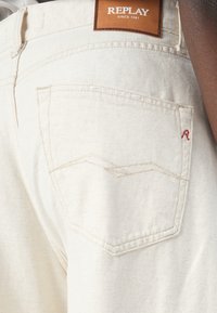 Witte denim jeans met een leren "REPLAY" label, subtiele stiksels en een onderscheidend ontwerp van de zak met een geborduurd rood "R."
