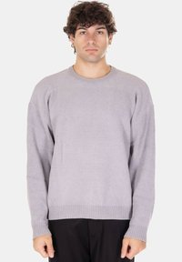 Maglione grigio chiaro lavorato a maglia con scollo rotondo e polsini a coste. Presenta un motivo a trama e una vestibilità rilassata, abbinato a pantaloni scuri.