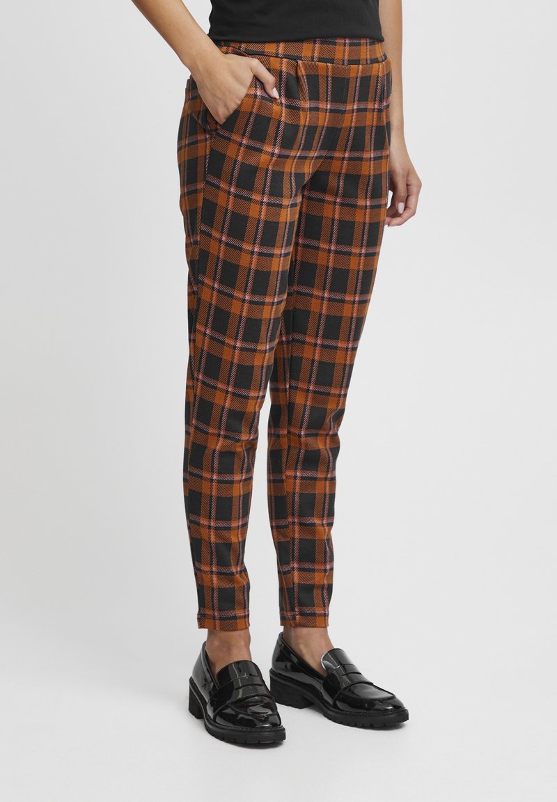 Plaid trousers in black, orange, and purple with a slim fit, featuring side pockets and a flat front waistband. Worn with black loafers.