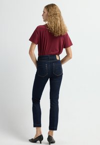 Tmavě modré džíny s vysokým pasem a fitted siluetou, spárované s vínově červeným tričkem s krátkým rukávem. Boty jsou černé s nízkým podpatkem.