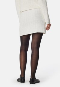 Vit texturerad tröja med en åtsittande, knälång kjol och svarta strumpbyxor. Svarta platta skor fulländar looken. Ren, minimal design.
