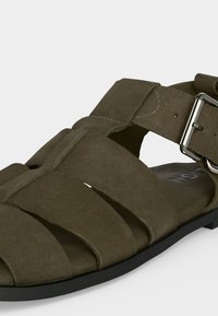 Ανδρικό σανδάλι από καστόρι ελιάς με πολλαπλούς ιμάντες και ασημένια κούμπωμα σε μαύρη σόλα.