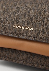 Brown textured handbag featuring a signature logo plate in gold, with a smooth tan leather accent at the bottom.