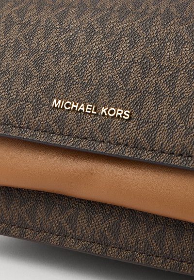 Sac à main texturé marron avec une plaque logo signature en or, associé à un accent en cuir lisse beige en bas.