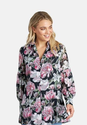 Camisa de botones floral con fondo negro y grandes peonías rosas y blancas. Mangas largas con un ajuste holgado y un ligero detalle de volantes.
