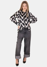 Blusa a zigzag in bianco e nero con scollatura rotonda e maniche lunghe, abbinata a jeans grigi a gamba larga e tacchi a spillo.