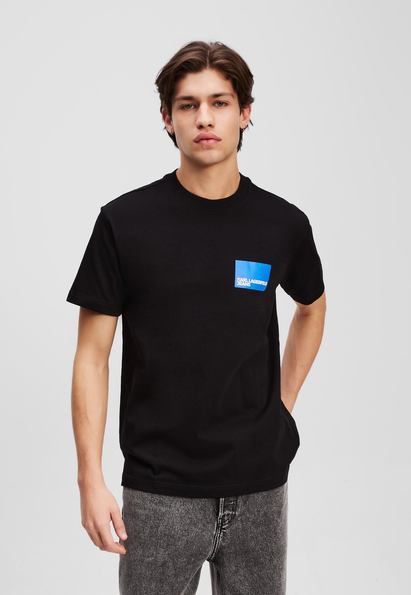 Melnas kokvilnas t-krekls ar apaļu kaklu, īsām piedurknēm, ar zilu taisnstūrveida kabatu ar baltu tekstu. Brīva piegriezuma stils.