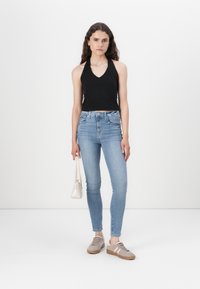 Melna halter top, gaiši zils skinny džinsus, pelēkas kedas ar rozā akcentiem un mazu baltu rokassomu uz vienkārša balta fona.