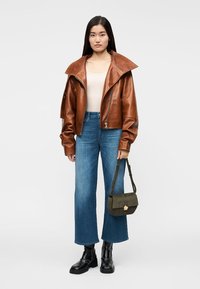 Giacca corta in pelle marrone con ampio colletto, abbinata a jeans a gamba dritta azzurri e stivali neri con plateau. Borsa a tracolla verde oliva.