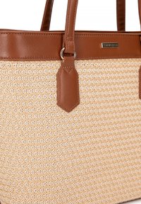 Beige geweven tas met een gestructureerd oppervlak, accenten van bruin leer, dubbele handvatten en een metalen logo plaat. Het heeft een gestructureerde vorm.