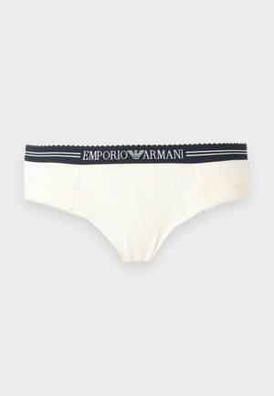 Slip blanc côtelé avec ceinture élastique noire arborant le logo "Emporio Armani" et des rayures décoratives sur un fond gris uni.